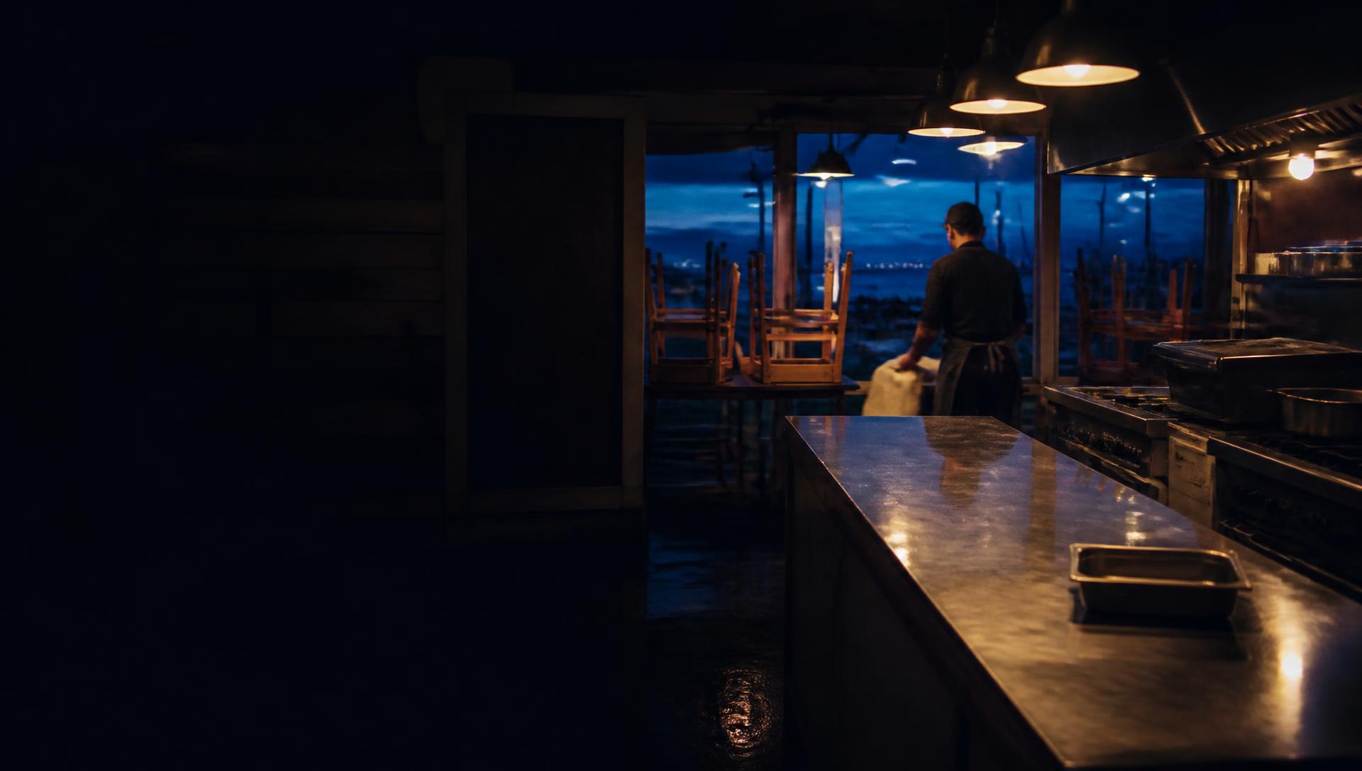 Family-run coastal restaurant kitchen at closing time, warm light on stainless surfaces
